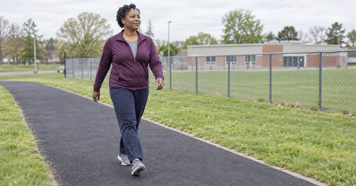Woman in a plum jacket walking on a paved community recreation track