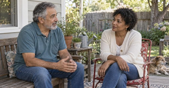 Older man and woman talking together on simple seats on a porch beside a garden.
